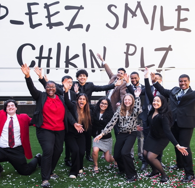 A group of Community Scholars in business attire celebrating with raised arms.
