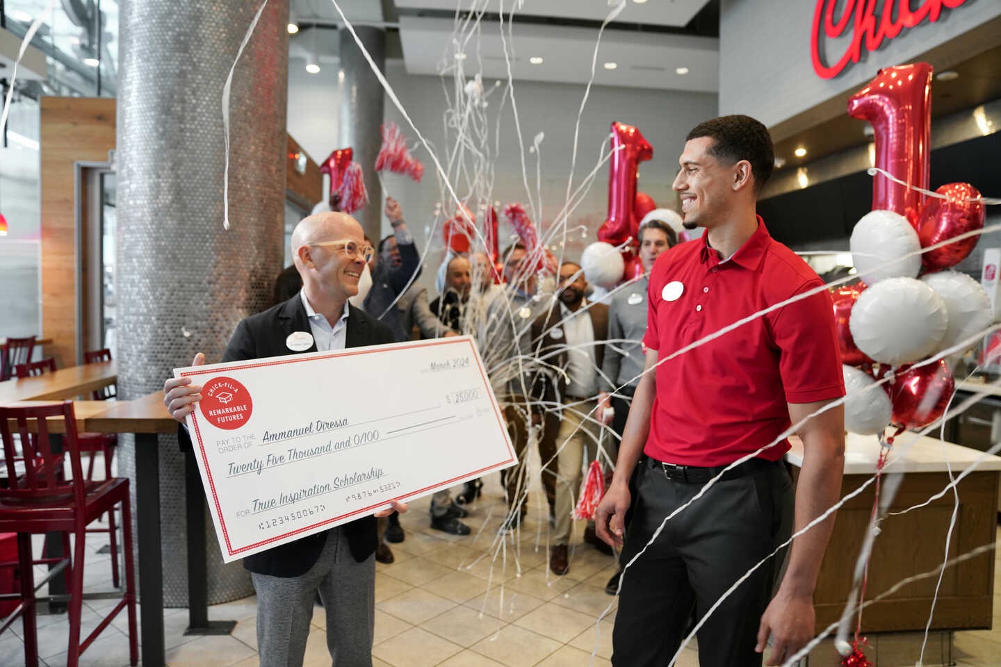 A festive celebration in a Chick-fil-A restaurant with a man holding a large check and balloons in the background.