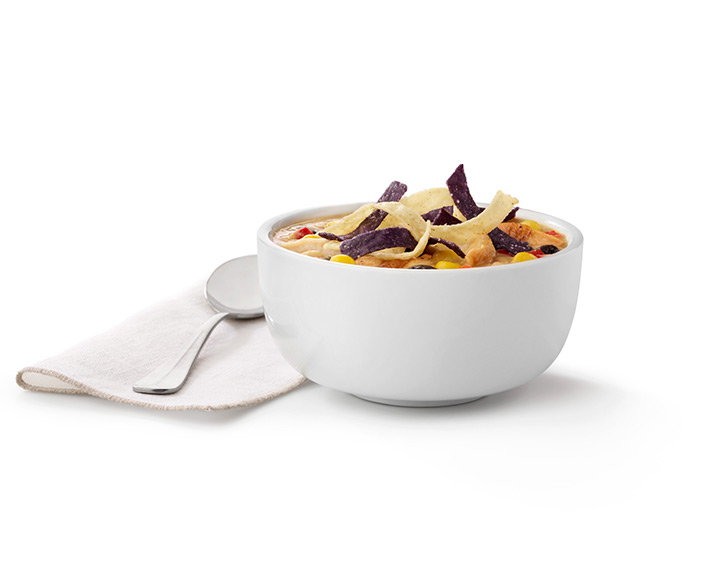 A bowl of Chicken Tortilla Soup next to a spoon on a napkin on a white tile background