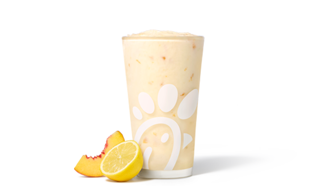 Peach Frosted Lemonade in a glass accompanied by a peach and a lemon slice.
