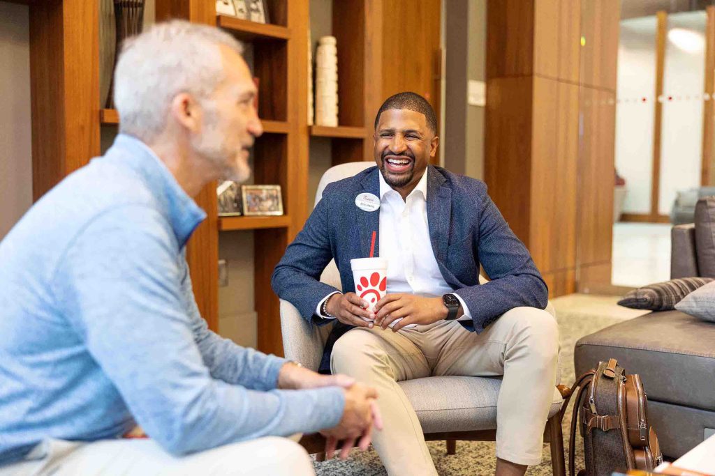 Chick-fil-A team member smiling while holding a beverage cup during a casual meeting in an office lounge.
