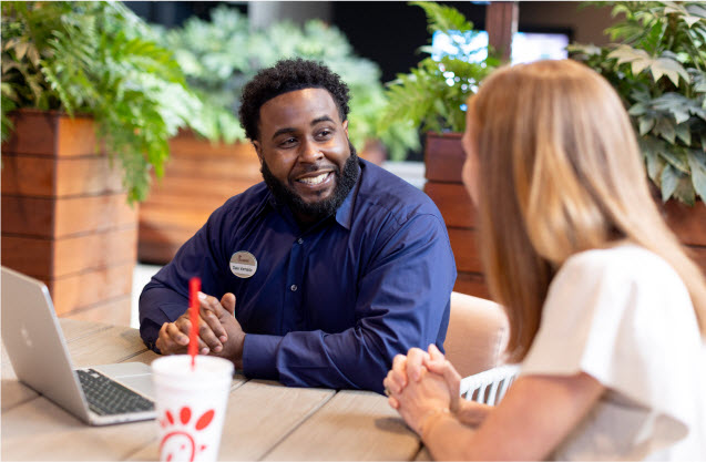 Two co-workers sitting at a table discussing work with a laptop open in front of them