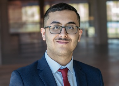 Headshot of Hasan with a blurred indoor background.