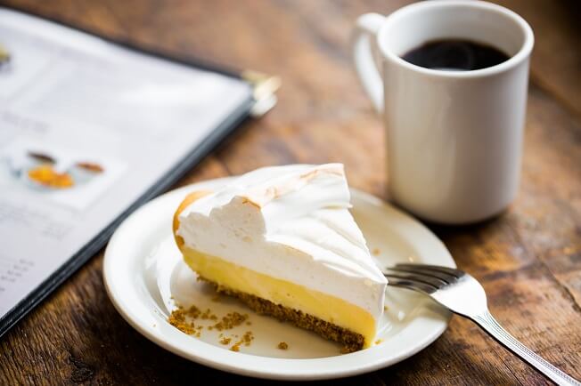 Slice of Lemon Pie sitting on a table next to a cup of coffee and a menu