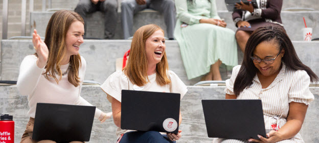 Three Chick-fil-A team members sitting on steps with laptops, smiling and collaborating during an informal work session.