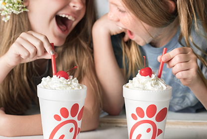Two people sitting together and smiling, each holding a straw poking into a Peach Milkshake