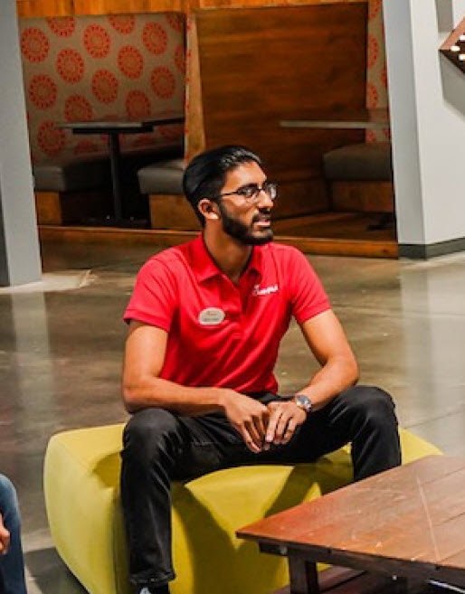 Chick-fil-A team member in red polo shirt seated in a casual workspace, engaged in conversation.