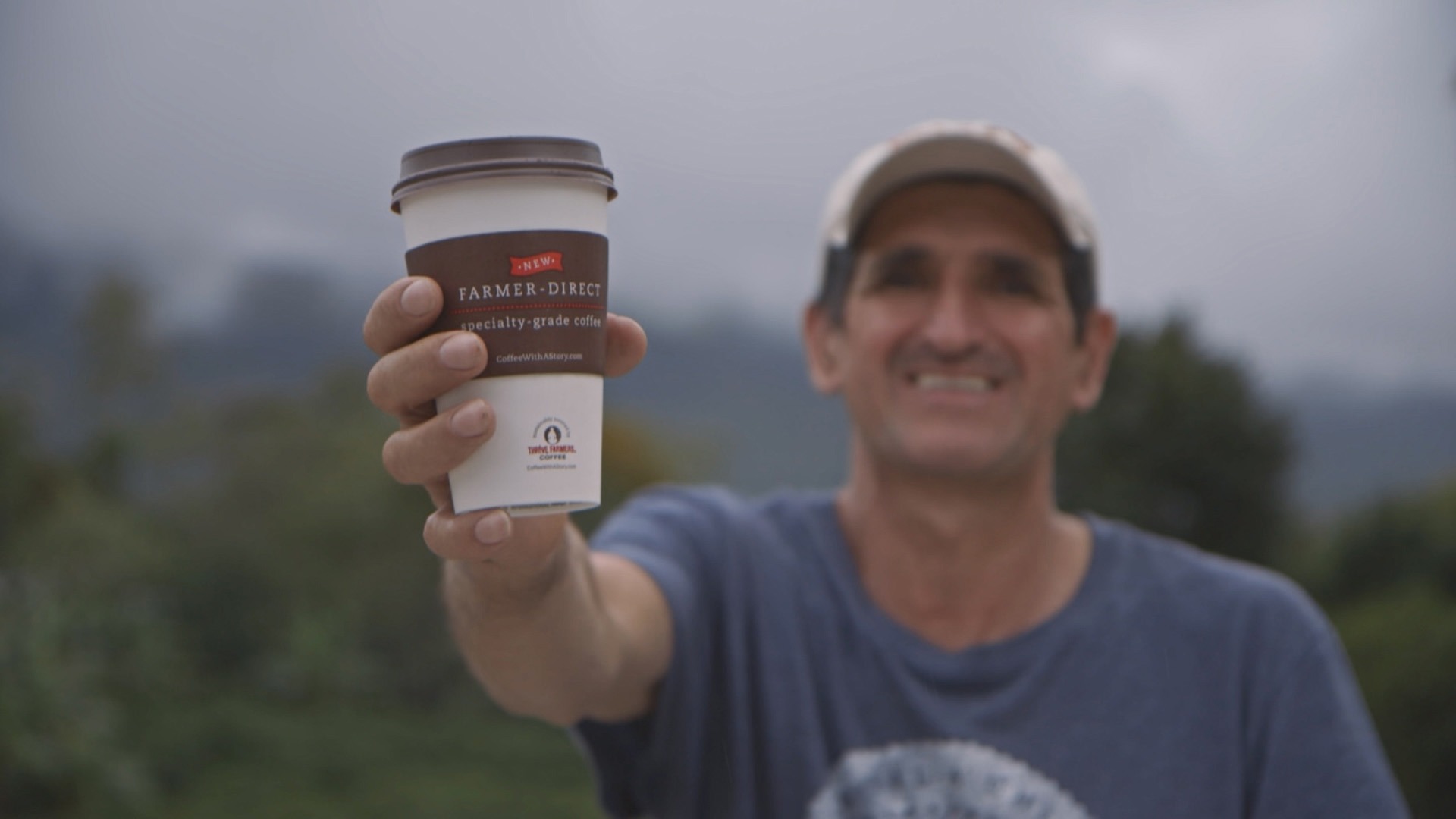 Man in a cap holding a coffee cup with a blurred natural background.