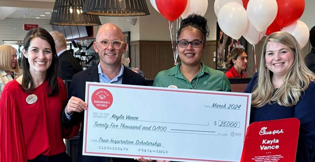 Four people in a Chick-fil-A holding a large scholarship check for $25,000 awarded to Kayla Vance.