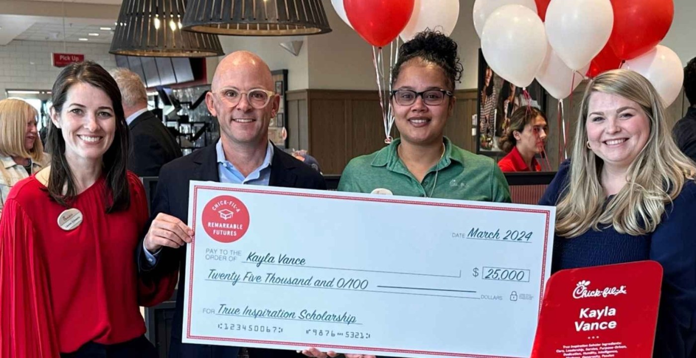 Four people in a Chick-fil-A holding a large scholarship check for $25,000 awarded to Kayla Vance.