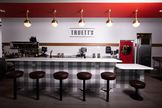 Truett's Chick-fil-A interior with a counter, red stools, pendant lamps, and the word "TRUETT'S" on the back wall.
