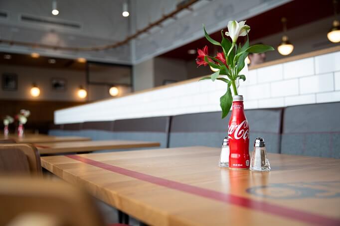 A Coca-Cola bottle holding flowers on a Truett's Chick-fil-A table, with salt and pepper shakers beside it.