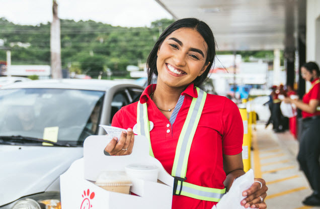 A Team Member standing outside a Chick-fil-A Restaurant smiling and holding a drink carrier
