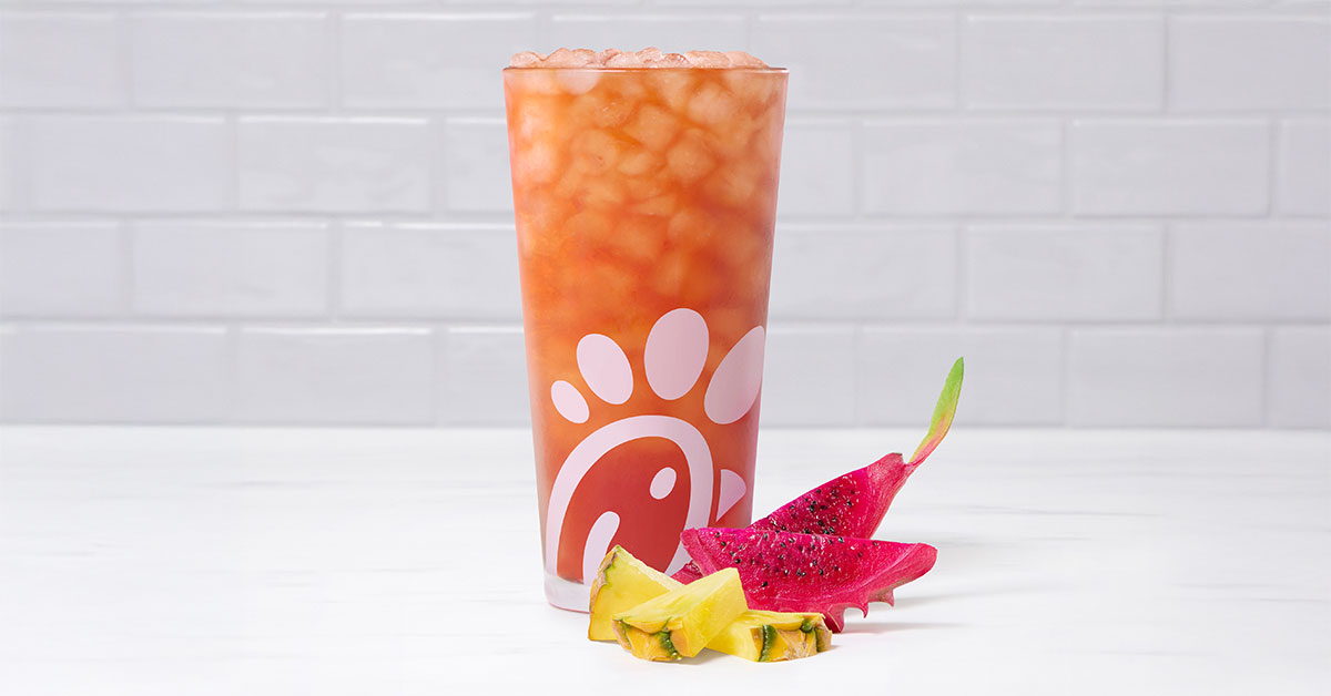 A glass of a Pineapple Dragonfruit Iced Tea by slices of pineapple and dragon fruit.