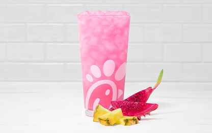 A glass of a Pineapple Dragonfruit Lemonade accompanied by slices of pineapple and dragon fruit.