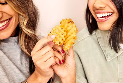 Two people smiling, holding a Waffle Fry and clinking them together