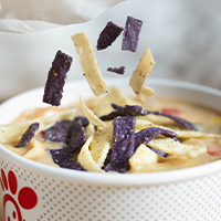 Tortilla strips being sprinkled into a cup of Chicken Tortilla Soup.