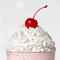 Closeup of whipped cream and cherry on top of a peppermint shake.