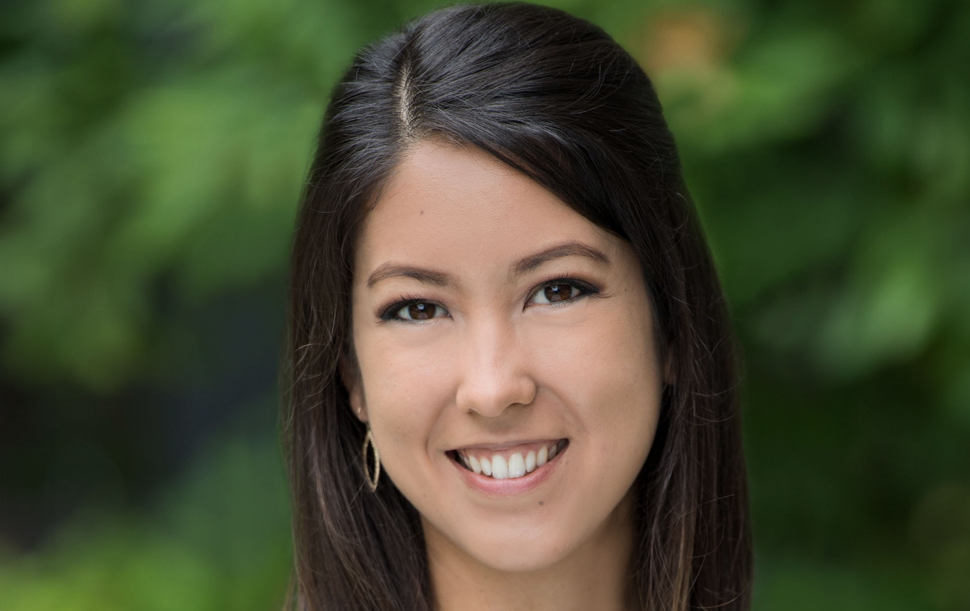 Professional headshot of Abbi Watkins with softly blurred green and yellow foliage background