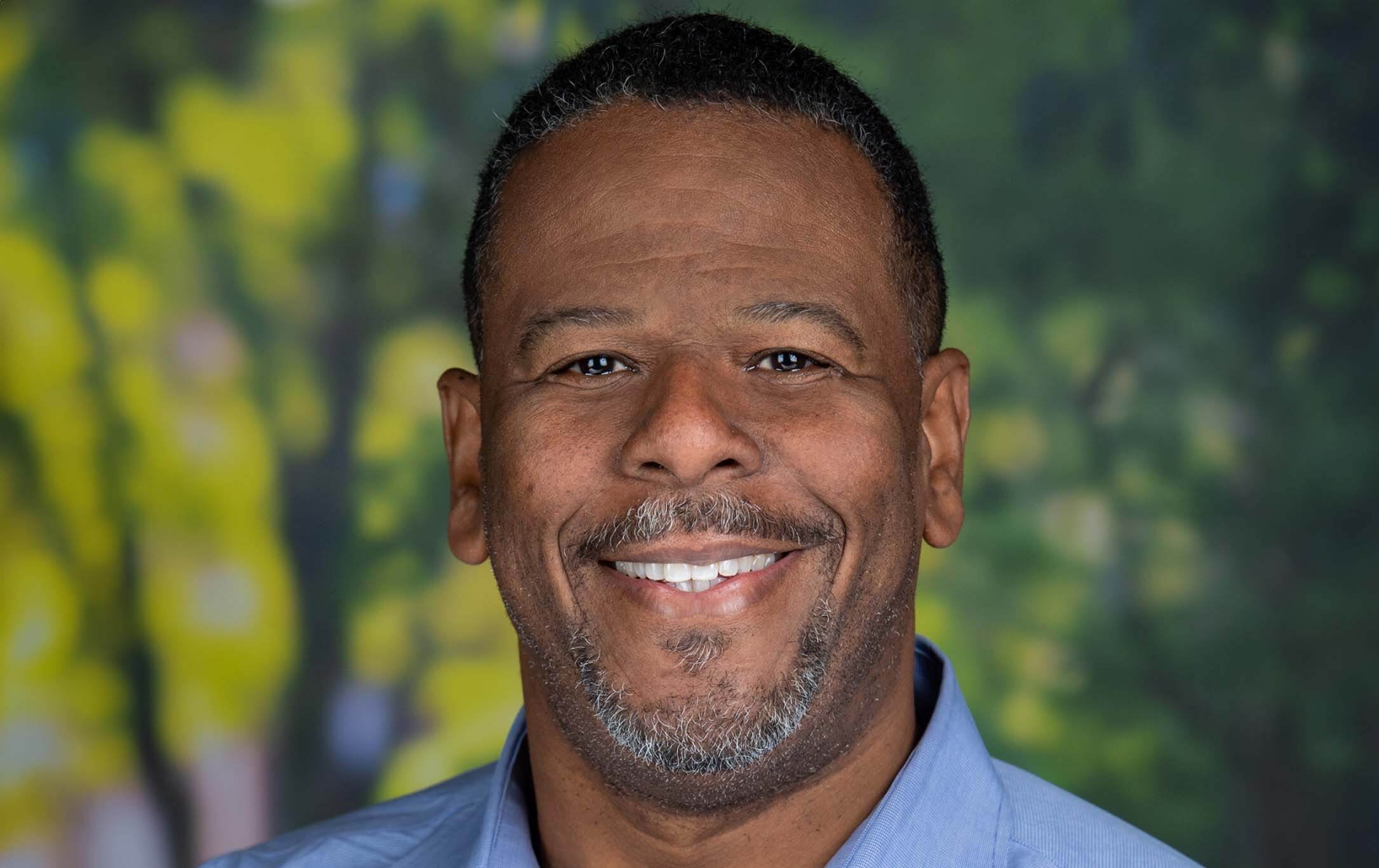 Professional headshot of  Corregan Brown with softly blurred green and yellow foliage background