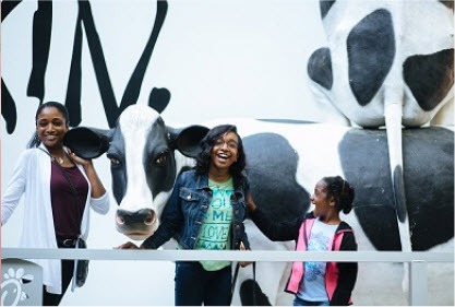 Three people smiling in front of a large black and white cow sculpture.