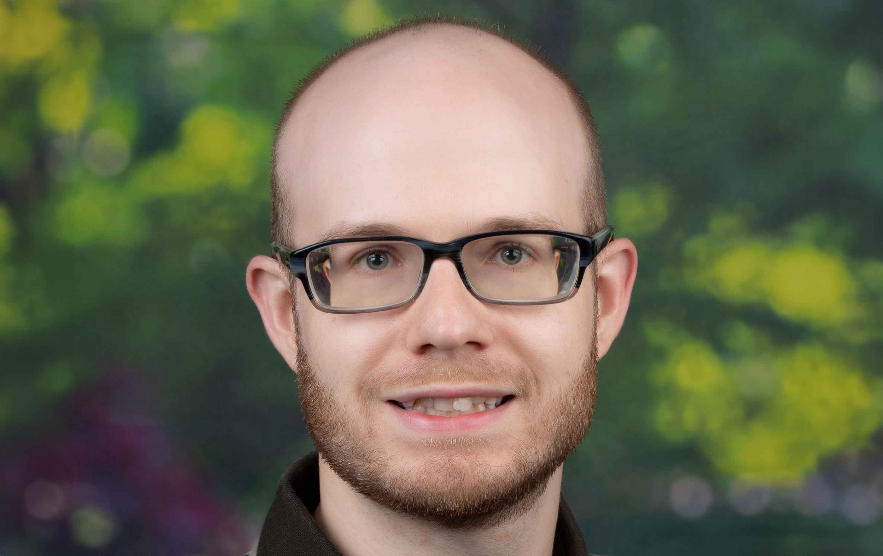 Professional headshot of Jake Wilson with softly blurred green and yellow foliage background