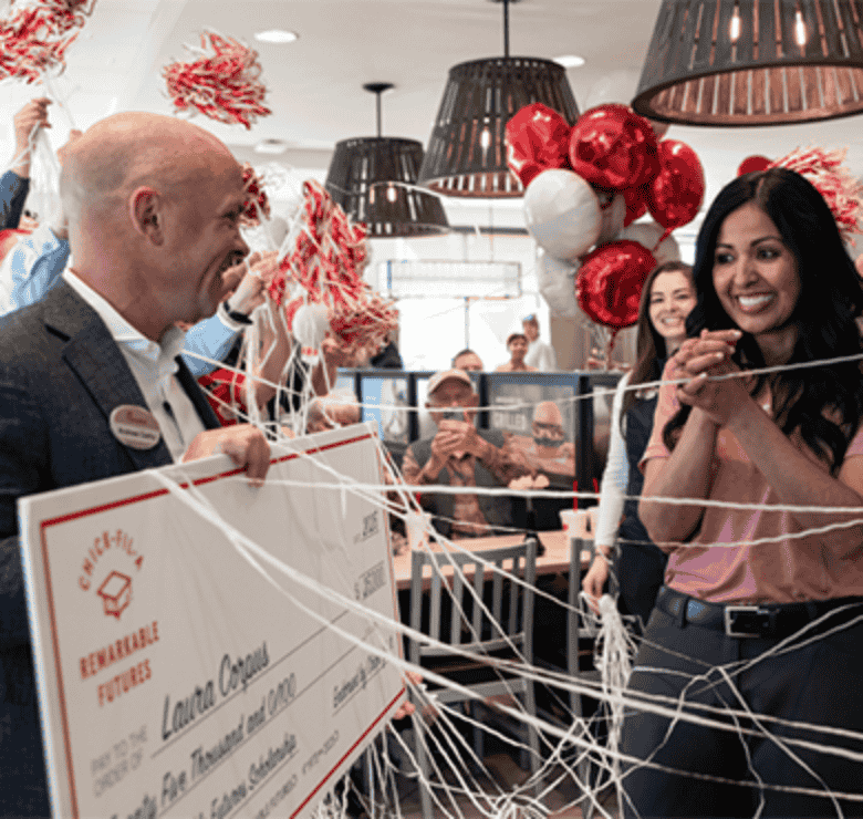 Chick-fil-A Team Member holding a large check and surrounded by other people and balloons
