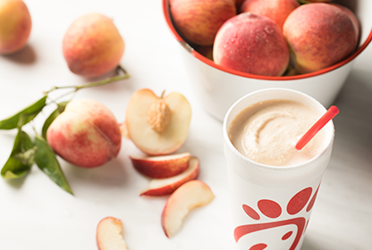 A Peach Milkshake on a table with a bowl of peaches and sliced peaches next to it