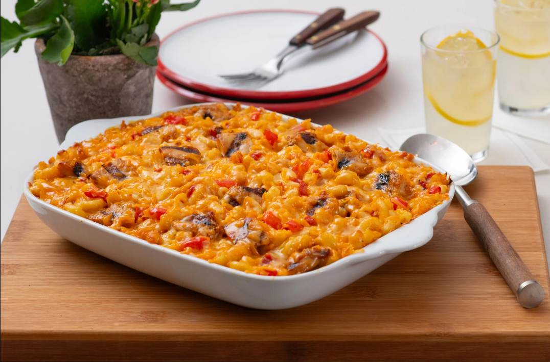 A platter of Southwest Mac and Cheese on a wooden cutting board with a serving spoon