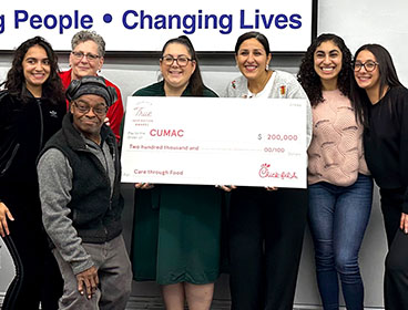 A group of people from the Center of United Methodist Aid to the Community (CUMAC) standing around a large check and smiling
