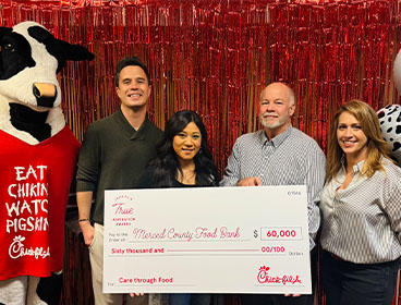 People from the Merced County Food Bank organization standing together smiling with a Chick-fil-A Cow and holding a large check