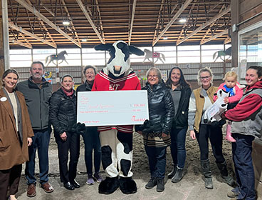 A Chick-fil-A Cow holding a large check with people from the Special Equestrians organization standing around him and smiling