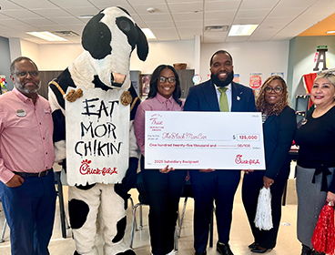 People from The Black Man Can, Inc. standing together with a Chick-fil-A Cow, holding a large check and smiling