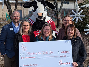 People from the Friends of the Topeka Zoo organization standing together smiling with a Chick-fil-A Cow and holding a large check