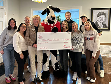 A Chick-fil-A Cow in the middle of a group of people from the Travis Manion Foundation, all standing together smiling and holding a large check