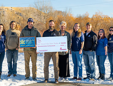 People from one of the category winner organiztions, Warriors & Quiet Waters Foundation, standing together outside and holding a large check
