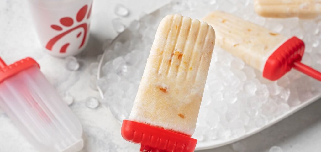 Creamy peach popsicles with red handles on ice.