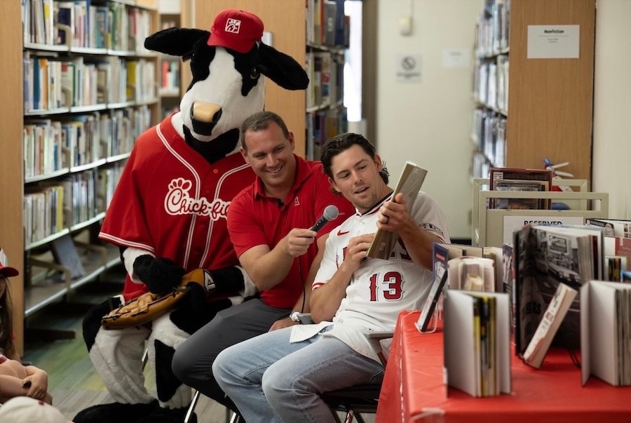 Chick-fil-A cow mascot joins a baseball player and announcer during a book reading at a public library.