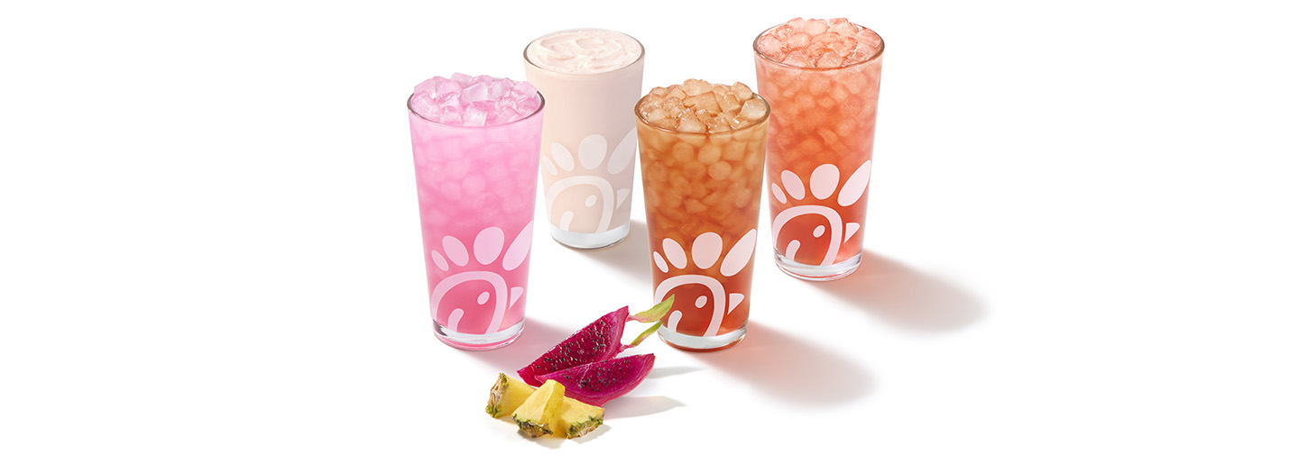 A glass of a Pineapple Dragonfruit Lemonade, Frosted Lemonade, Iced Tea and Sunjoy with pieces of pineapple and dragonfruit next to them on a gray background
