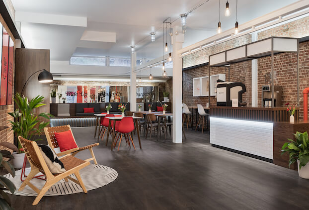 A modern, stylish lounge space with cozy seating areas, brick walls, artwork, and dining tables, designed with a warm and inviting atmosphere.