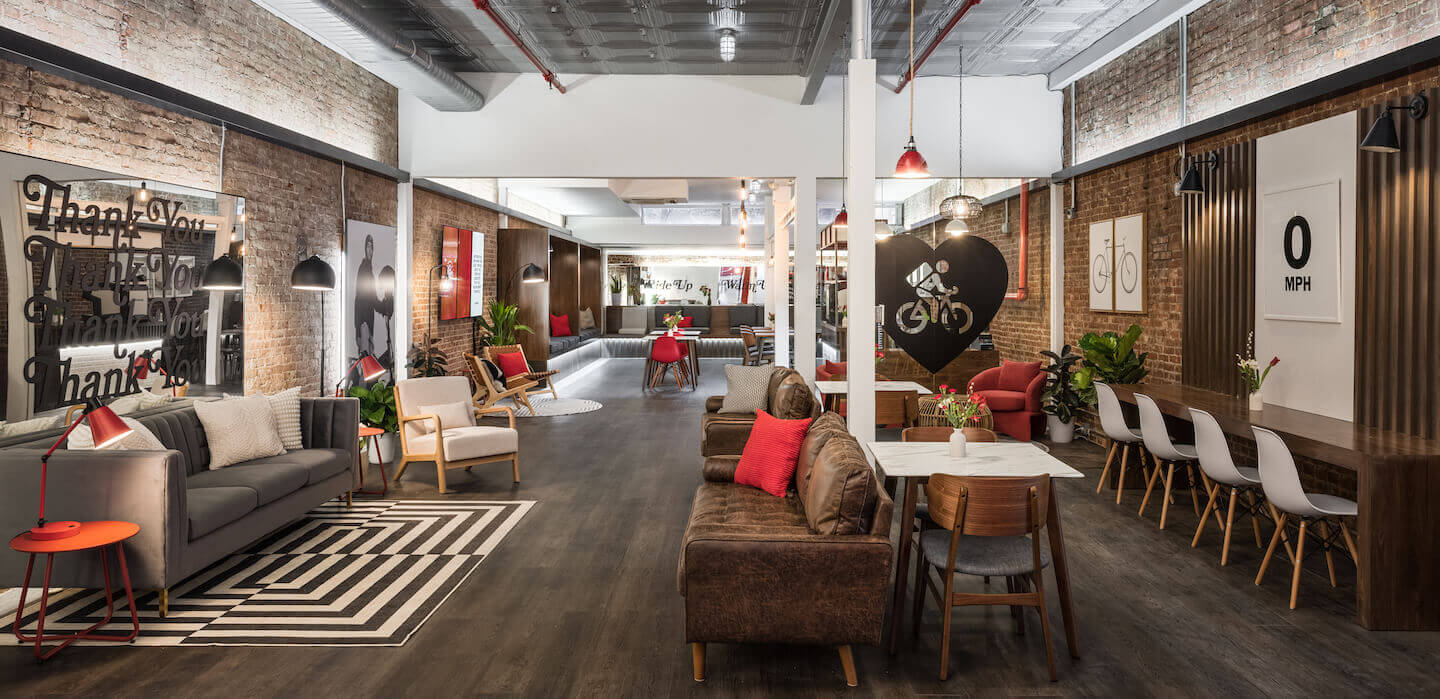 A modern, stylish lounge space with cozy seating areas, brick walls, artwork, and dining tables, designed with a warm and inviting atmosphere.