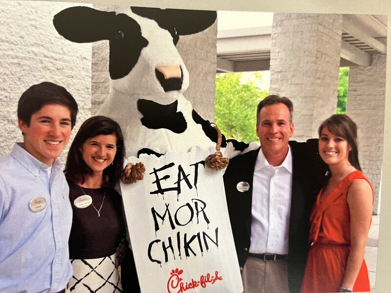 People posing with a person in a cow costume holding a sign that says "EAT MOR CHIKIN."