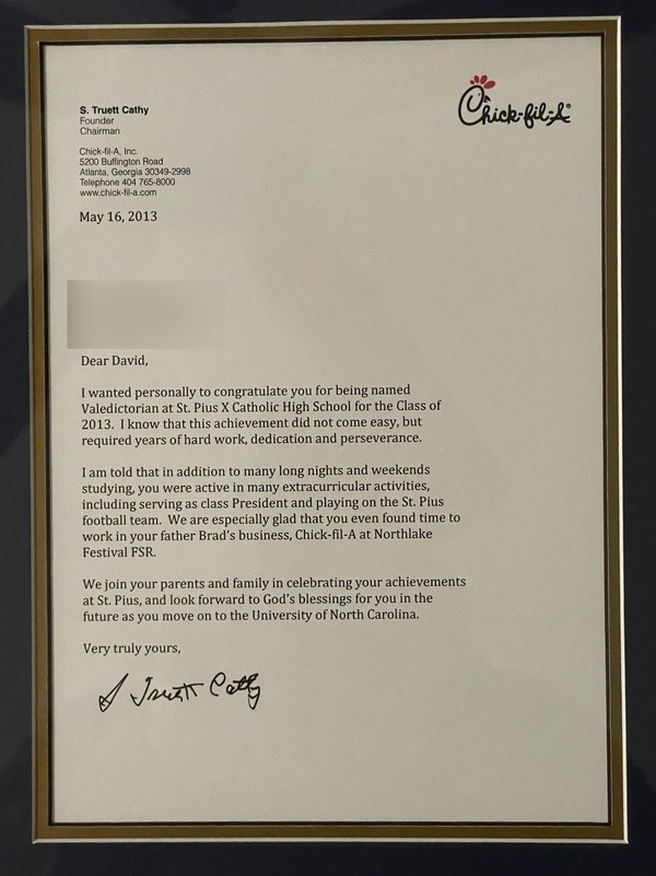 Framed congratulatory letter from S. Truett Cathy of Chick-fil-A to a student named David.

Transcribed Text:

S. Truett Cathy
Founder
Chairman
Chick-fil-A, Inc.
5200 Buffington Road
Atlanta, Georgia 30349-2998
Telephone 404 765-8000
www.chick-fil-a.com

May 16, 2013

Dear David,

I wanted personally to congratulate you for being named Valedictorian at St. Pius X Catholic High School for the Class of 2013. I know that this achievement did not come easy, but required years of hard work, dedication and perseverance.

I am told that in addition to many long nights and weekends studying, you were active in many extracurricular activities, including serving as class President and playing on the St. Pius football team. We are especially glad that you even found time to work in your father Brad’s business, Chick-fil-A at Northlake Festival FSR.

We join your parents and family in celebrating your achievements at St. Pius, and look forward to God’s blessings for you in the future as you move on to the University of North Carolina.

Very truly yours,

[S. Truett Cathy Signature]