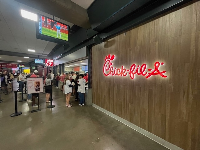 Fans line up at a Chick-fil-A concession stand inside a baseball stadium.