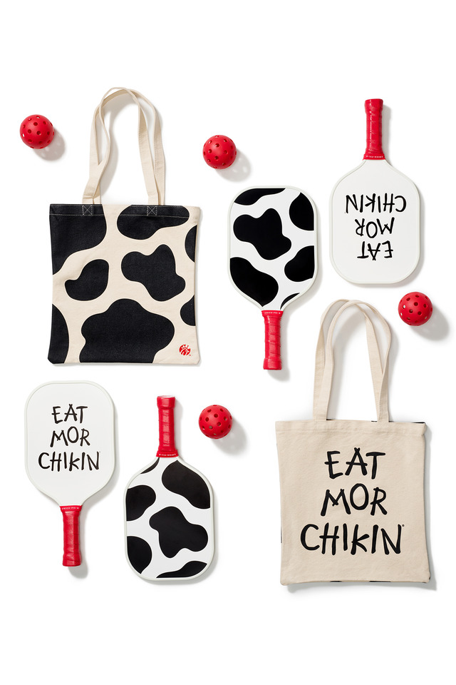 Cow print and "EAT MOR CHIKIN" themed tote bags and pickleball paddles with red pickleballs.