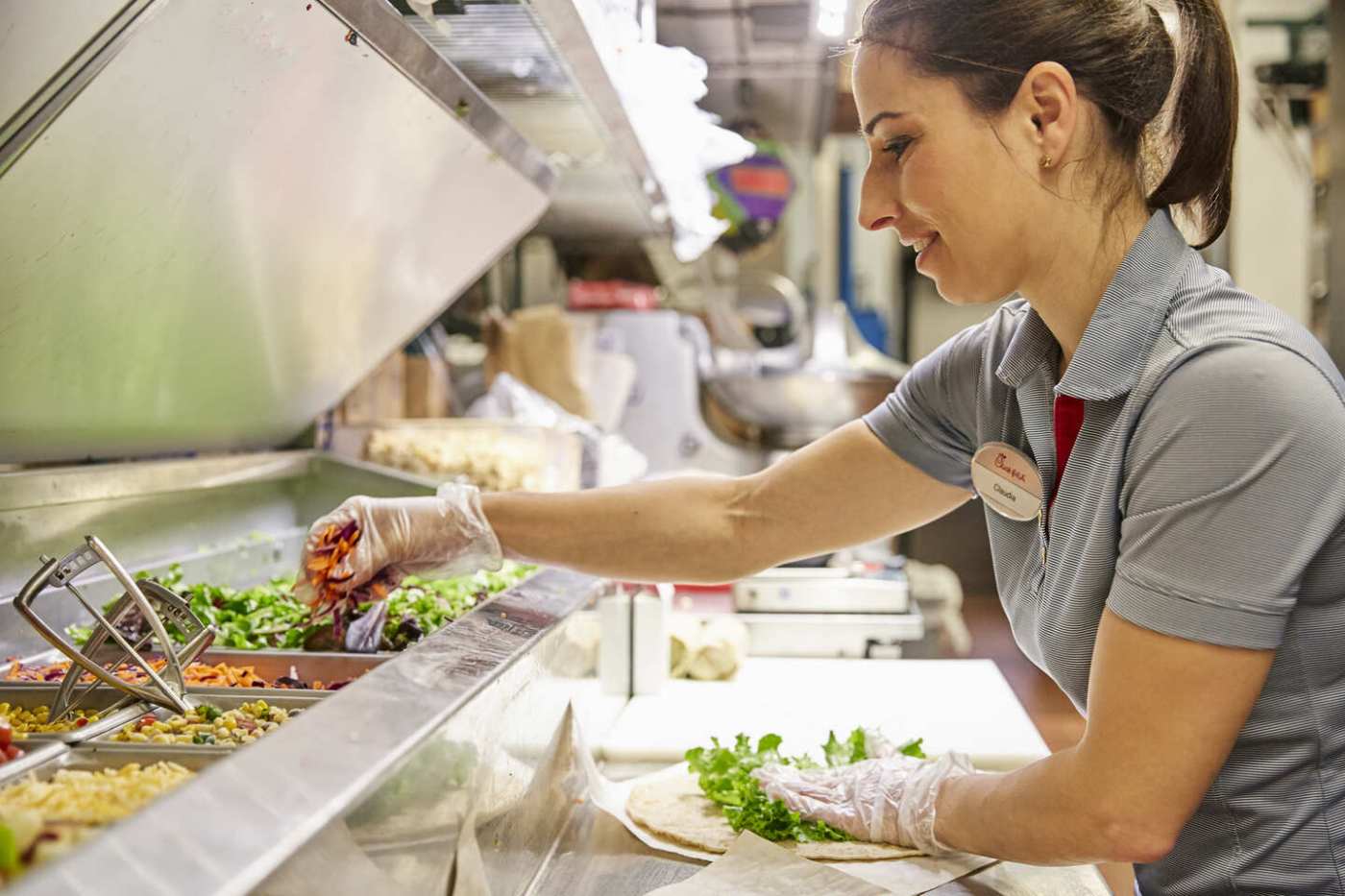 Chick-fil-A team member preparing a wrap in a restaurant kitchen with various fresh ingredients.