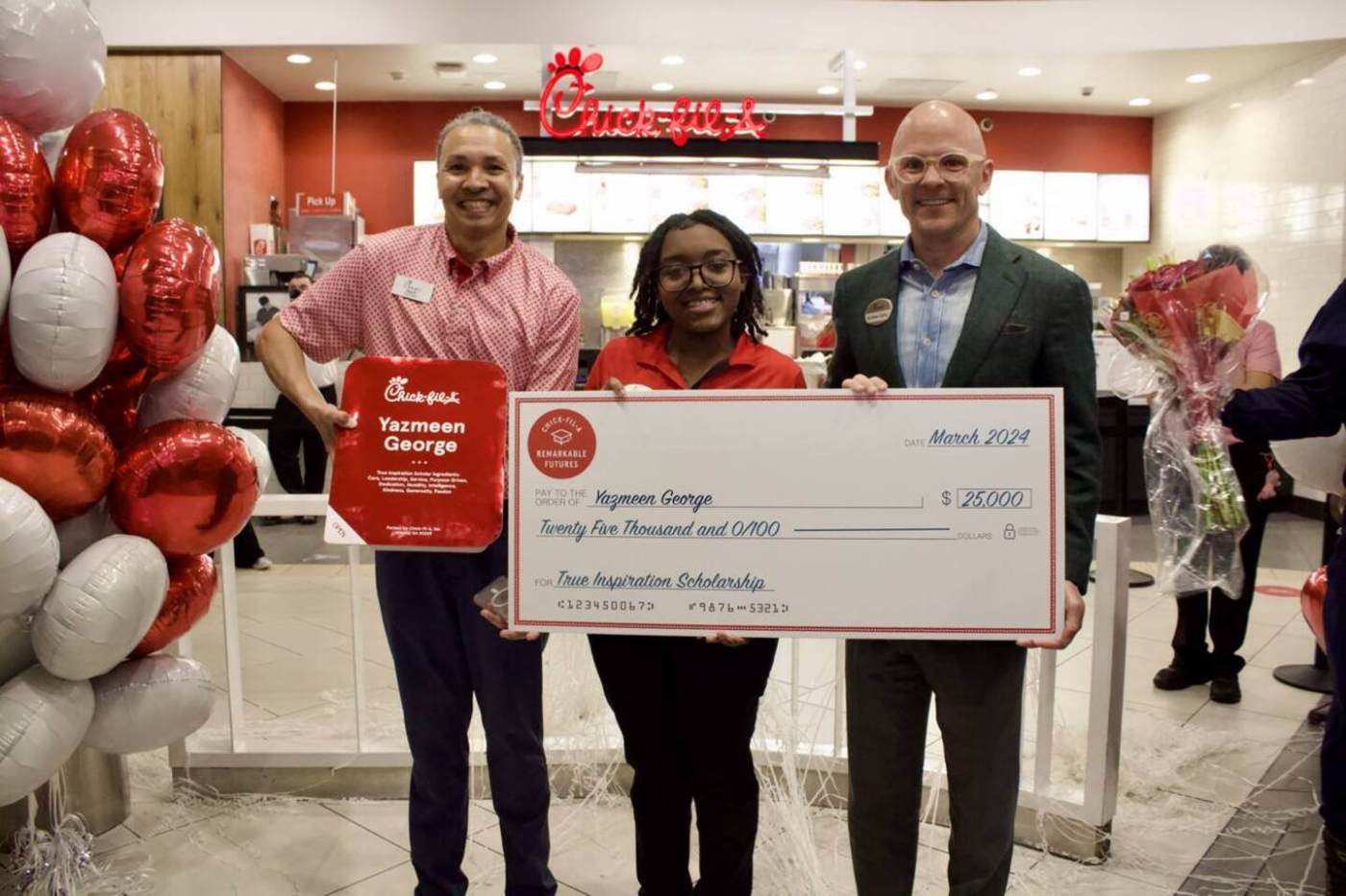 Three people holding a large ceremonial check inside a Chick-fil-A restaurant.