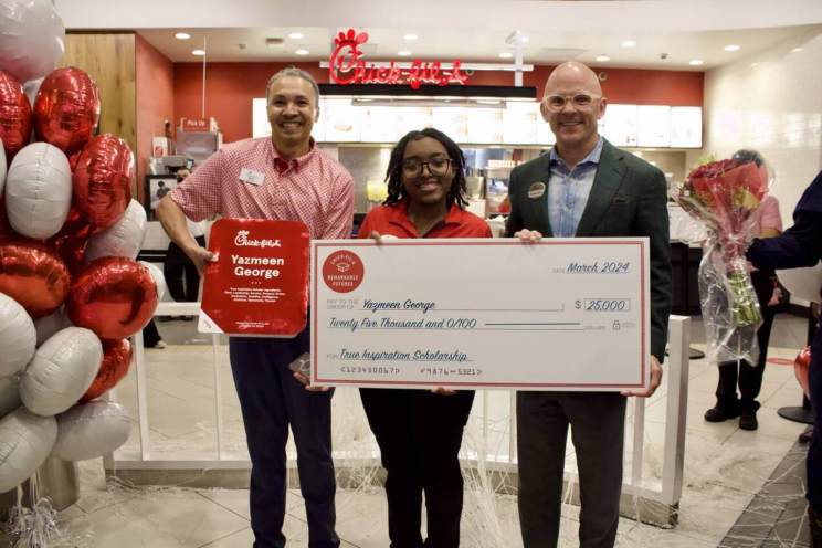 Three people holding a large ceremonial check inside a Chick-fil-A restaurant.