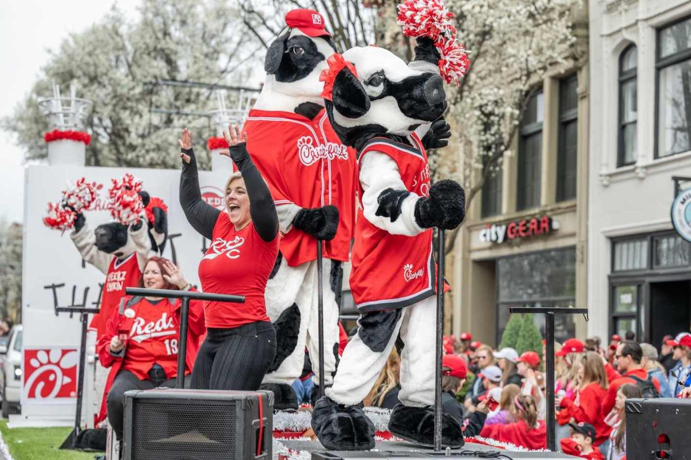 Chick-fil-A cow mascots in red jerseys and fans cheer during a parade float celebration.