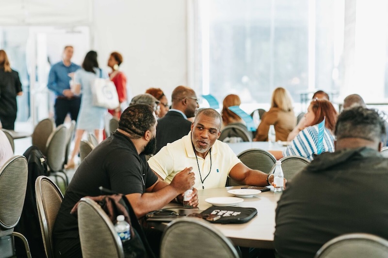 2025 Impact Accelerator Conference Attendees conversing with large windows in the background.